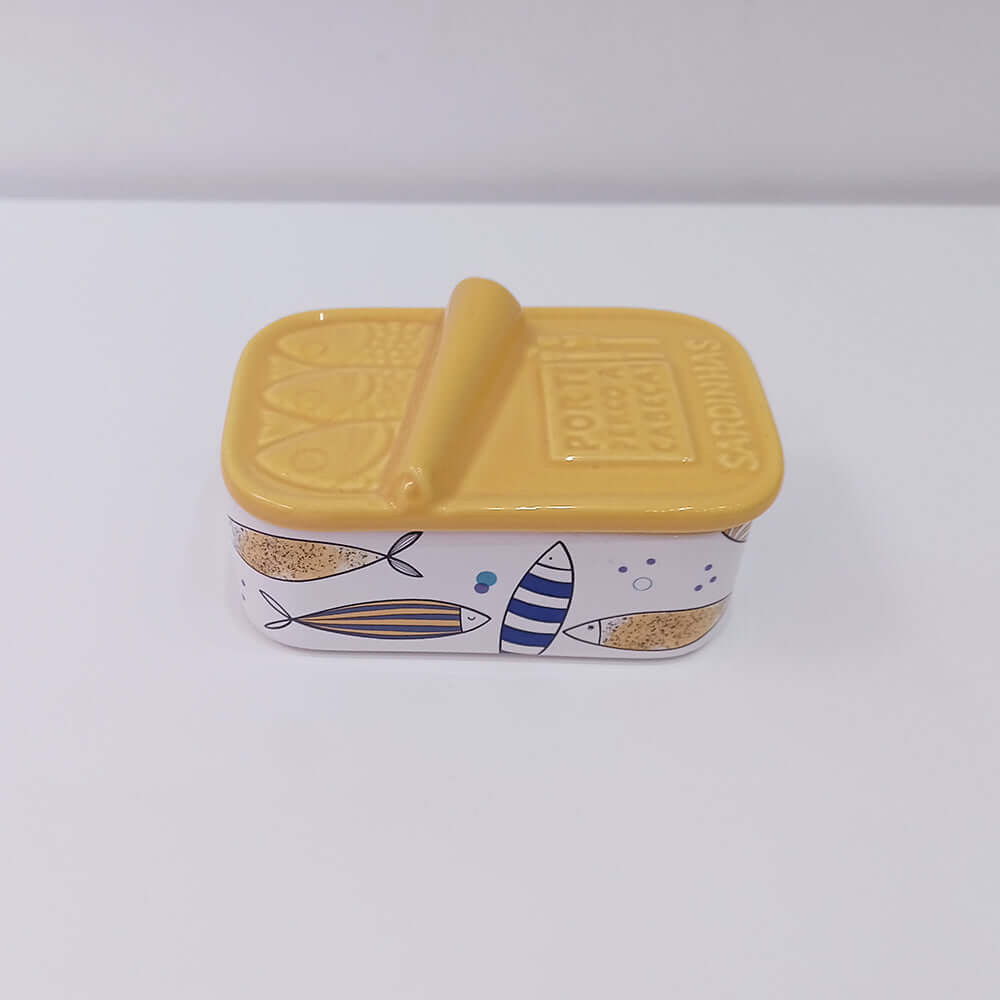 Caixa de cerâmica amarela em formato de lata de sardinha com peixes desenhados.