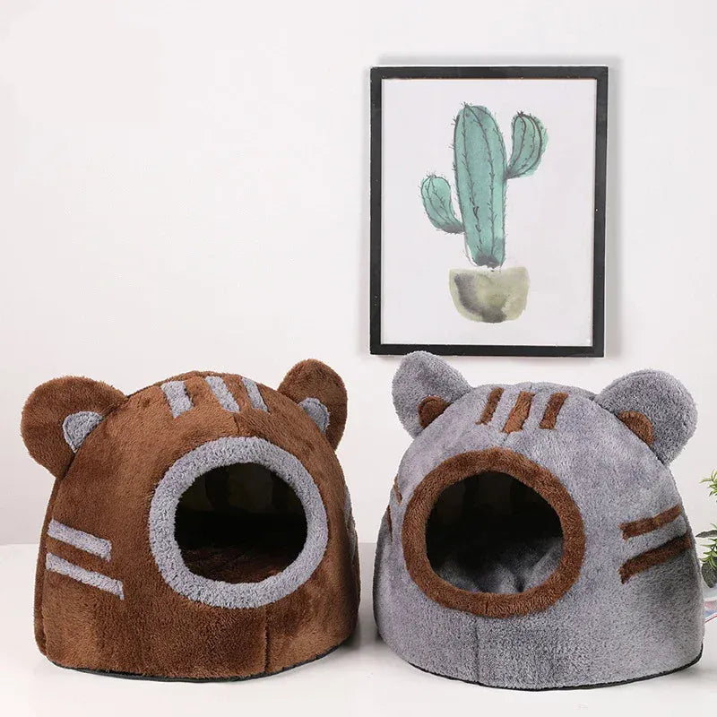 Two cat-shaped pet beds, one brown and one gray, on a white surface with a cactus painting in the background.